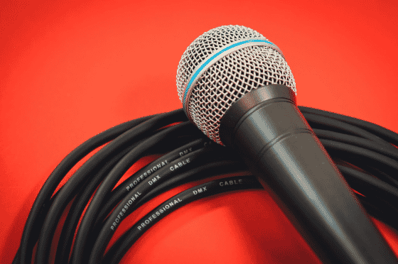 Close-up of a mic cable wrapped around a black dynamic microphone on a red background, showcasing high-quality mic cables for live performances, recording, and AUX and mic cable setups