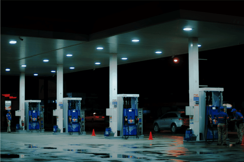 Modern gas station at night, brightly illuminated with overhead lights, showcasing multiple fuel pumps and an organized layout. Station employees in uniforms are visible, highlighting active service and maintenance. Traffic cones ensure safety, and the clean, well-maintained environment underscores the importance of durable low-voltage gas and oil-resistant cables for efficient and safe operations