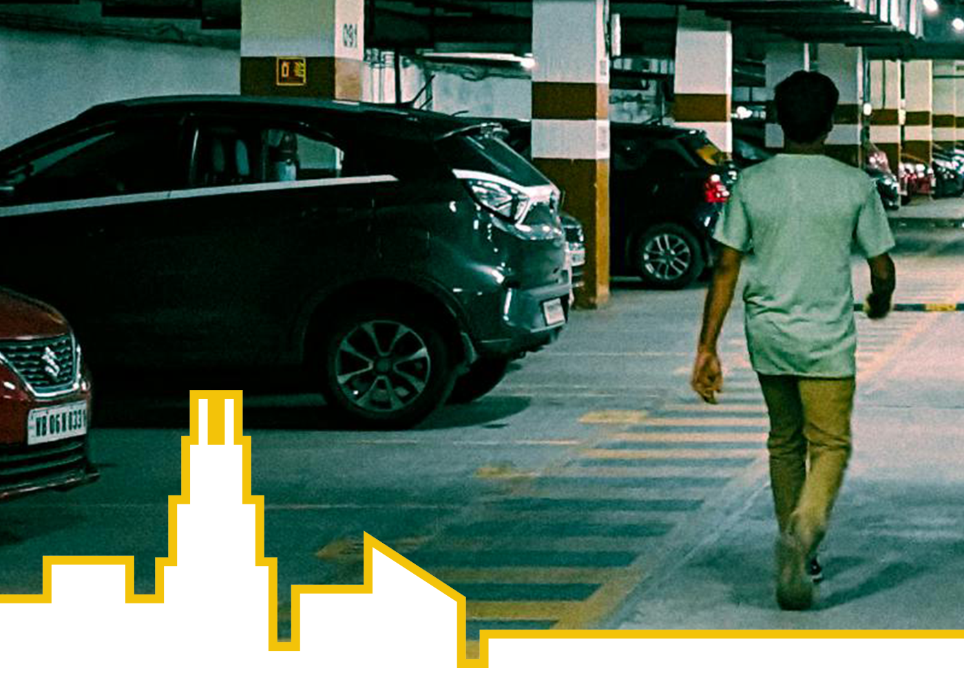 A person walks away from the camera through an indoor parking garage, with several parked cars on either side. The floor has painted pedestrian crossing lines, and the lighting is dim with concrete pillars throughout. A stylized yellow-and-white city skyline graphic overlays the bottom of the image.
