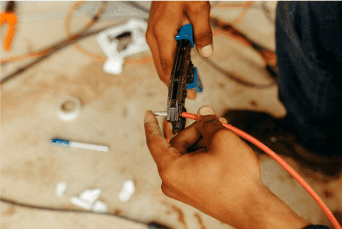 Technician using a crimping tool to terminate a red fiber optic cable on-site, showcasing the precision required in field-terminated fiber optic solutions. This image illustrates the manual process involved in field termination, emphasizing the customization and adaptability of this approach for network infrastructure projects
