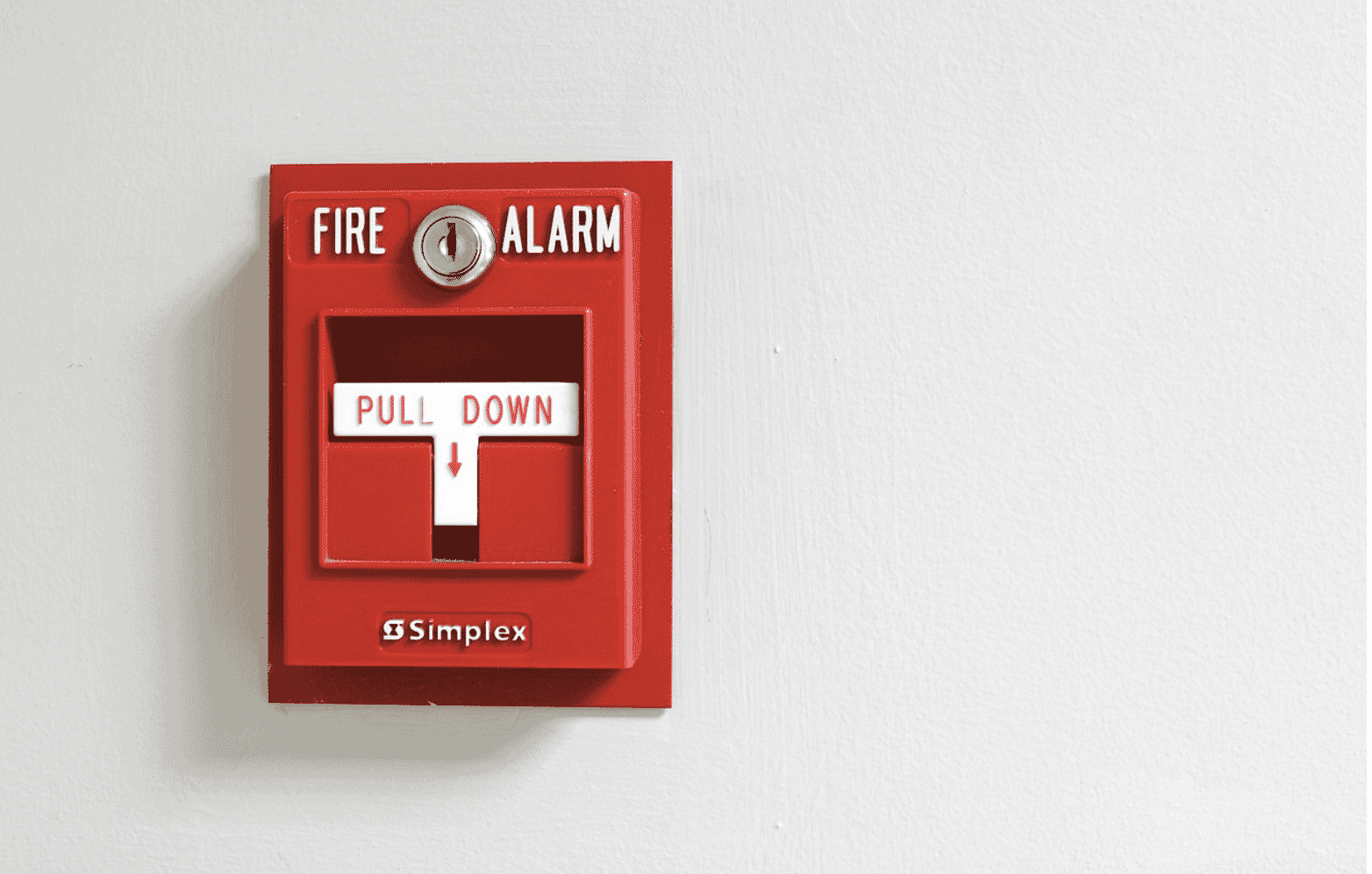 A red fire alarm pull station mounted on a white wall manually activates the fire alarm system. This system would involve fire alarm cables and wiring for proper installation. Depending on the installation needs, fire alarm systems may use stranded wire or pre-terminated fiber. Proper cable shielding is important for reducing interference across the types of fire alarm wiring used