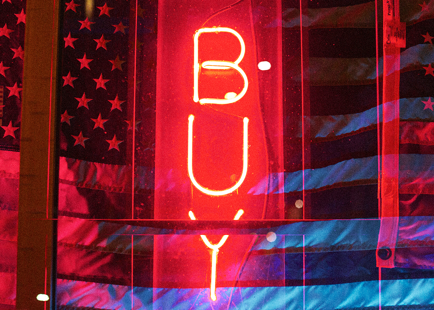 Bold red neon “BUY” sign layered over an American flag, symbolizing Buy American initiatives, domestic manufacturing, and U.S.-made product sourcing.