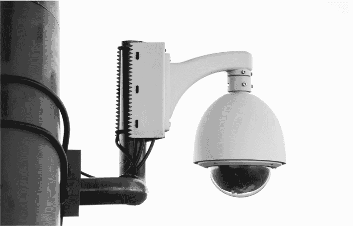 Close-up of a wired CCTV camera mounted on a pole, illustrating components of a wired security camera system. The setup includes a camera wire and connections that align with a Cat 6 wiring guide, as well as the attaching of coaxial cable connector processes for secure surveillance installations