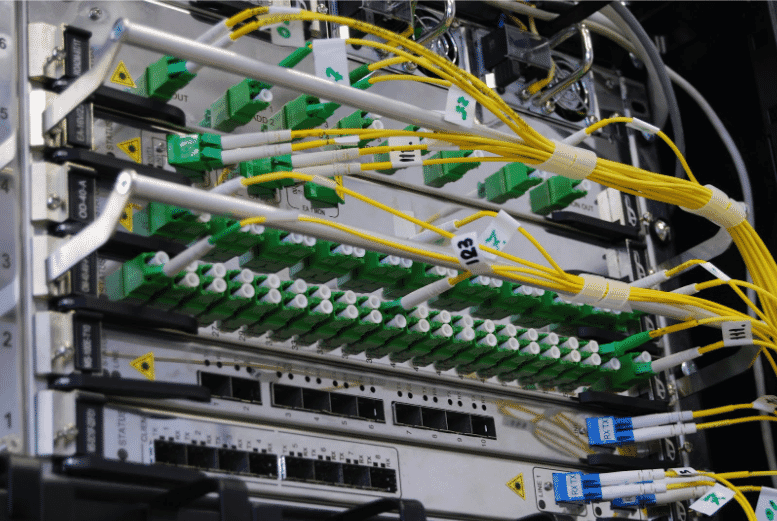 The image shows the installation of fiber optic cables in a network rack. The setup includes yellow fiber optic cables and connectors, displaying various organized cables for fast data transfer