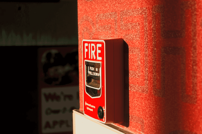Red wall-mounted fire alarm pull station with clear instructions, an essential component of an armored fire alarm cabling system, highlighted by sunlight to ensure high visibility and quick access in emergencies