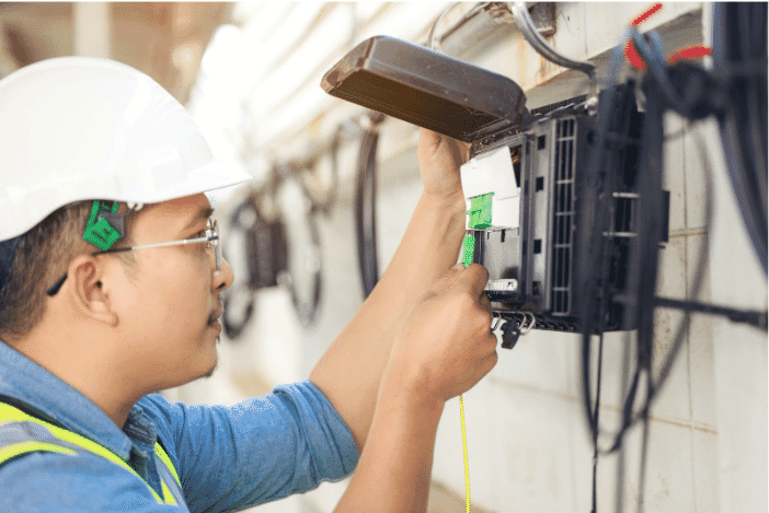 A technician in a hard hat working with an outdoor wire and cable connection. The setup likely includes RG6 coax cables, RG59 cables, and other RG cables, essential for reliable data transmission in outdoor environments