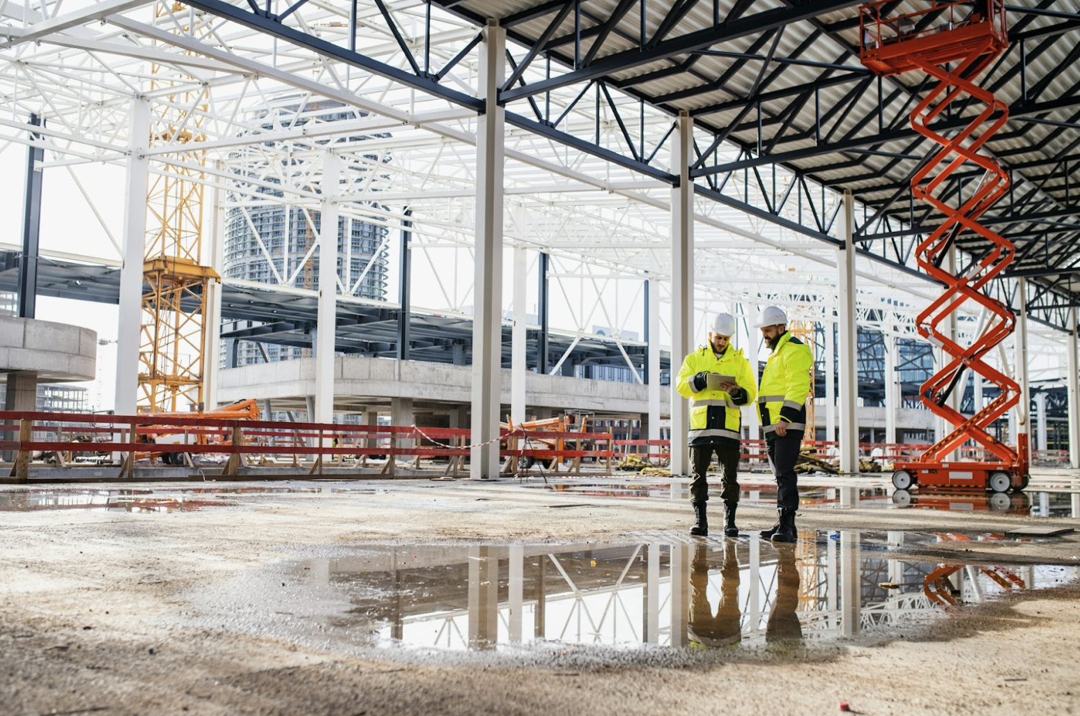 Engineers reviewing plans at a commercial outdoor construction site with standing water, illustrating real-world moisture exposure conditions that require water resistant wire and cable with UV-rated jackets and wet-location performance.