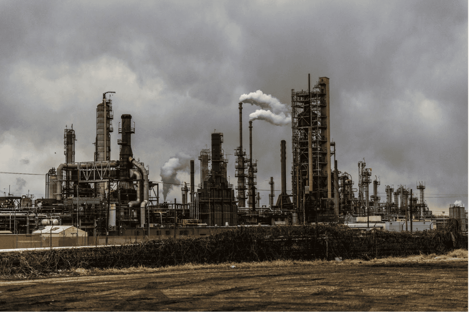 ndustrial oil refinery emitting smoke under a cloudy sky, representing a harsh environment where durable gas and oil cables, petroleum-resistant wiring solutions, and oil-resistant industrial cables are essential. High-performance petroleum and chemical-resistant industrial cables ensure safety and efficiency in demanding conditions