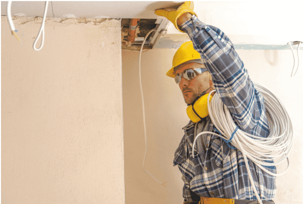 Electrician installing low-smoke fire cables in a building, preparing the space for fire life safety systems. The image illustrates the use of high-performance fire safety wiring, including fire-rated safety wiring and fire alarm system cables, essential for maintaining functionality during emergencies. The installation of emergency communication cables ensures reliable system performance during hazardous conditions