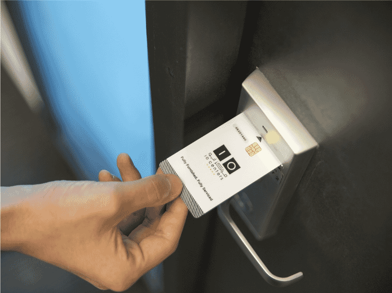 Close-up of a person's hand inserting a keycard into an electronic door lock, illustrating secure access control in a modern office or business environment. The keycard features a chip and branding for 'IO Centers,' emphasizing the use of advanced technology for workplace security and restricted access management