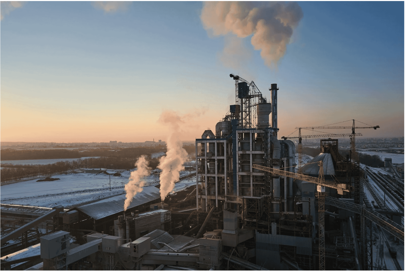 Industrial plant with cranes and smokestacks at sunrise, highlighting the importance of reliable UST cables in industrial infrastructure