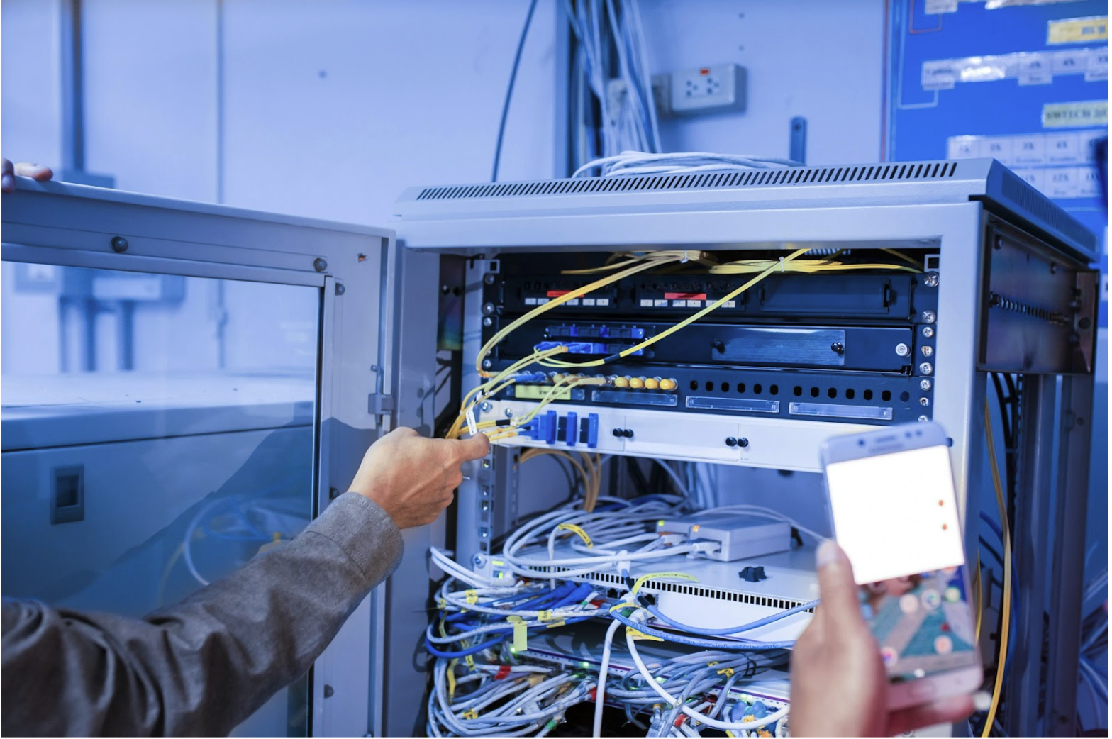 Technician organizing Ethernet and fiber cables inside a network rack, illustrating structured cabling systems and color-based cable identification in commercial network environments