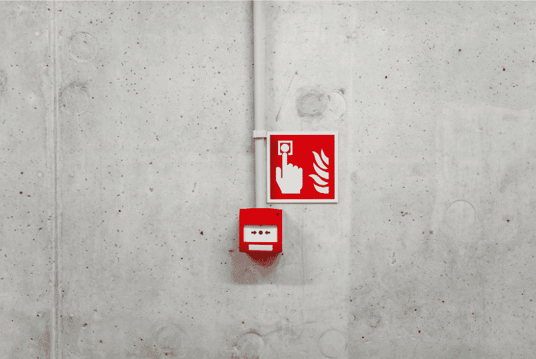 Fire alarm manual call point and signage on a concrete wall, highlighting the importance of 2-hour fire-rated cables in maintaining operational fire safety systems during emergencies