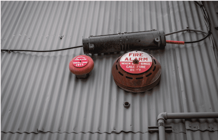 Industrial fire alarm system mounted on corrugated metal siding, highlighting the importance of 2-hour fire-rated cables for maintaining electrical integrity and fire safety in critical environments