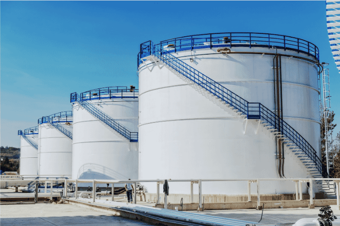 Large white fuel storage tanks with blue railings and industrial piping, representing the critical infrastructure of fuel storage facilities that benefit from high-performance UST electrical wiring designed for oil and chemical resistance to ensure safety and operational efficiency