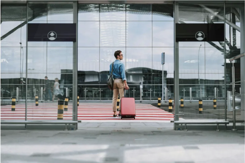 Traveler with a suitcase waiting outside automatic sliding entrance doors at an airport terminal, the type of low-voltage controlled door hardware wired with access control cable