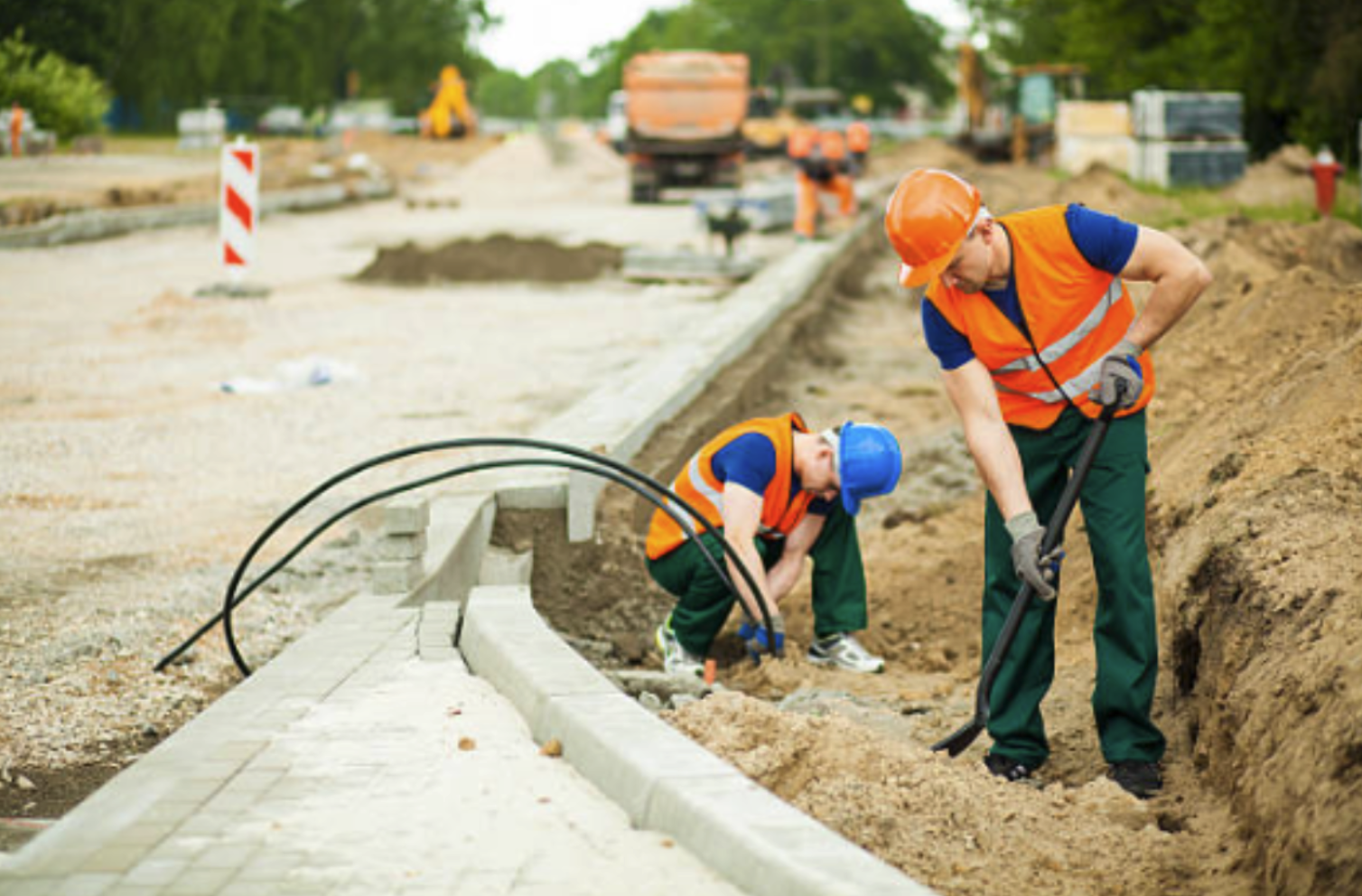 Workers installing underground cable in a trench for direct burial in commercial construction environment.