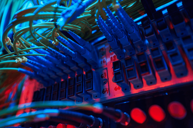 Close-up of a network panel with blue and yellow fiber optic cables connected to labeled ports, illuminated by blue and red lighting, illustrating single mode and multimode fiber optic technology in a high-speed data transmission setup