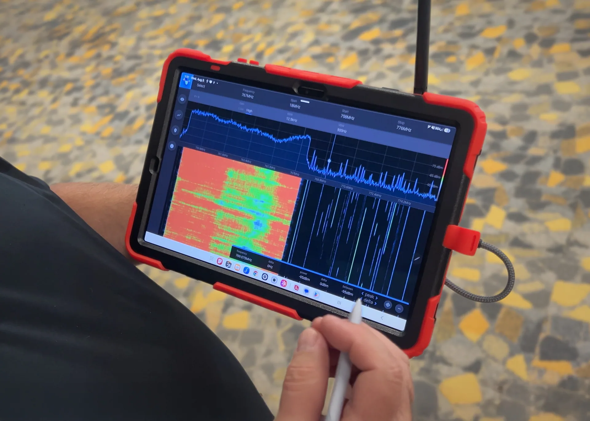Windy City Wire technician using a tablet-based RF spectrum analyzer to perform ERCES public safety in‑building grid testing, with spectrum and waterfall graphs visible