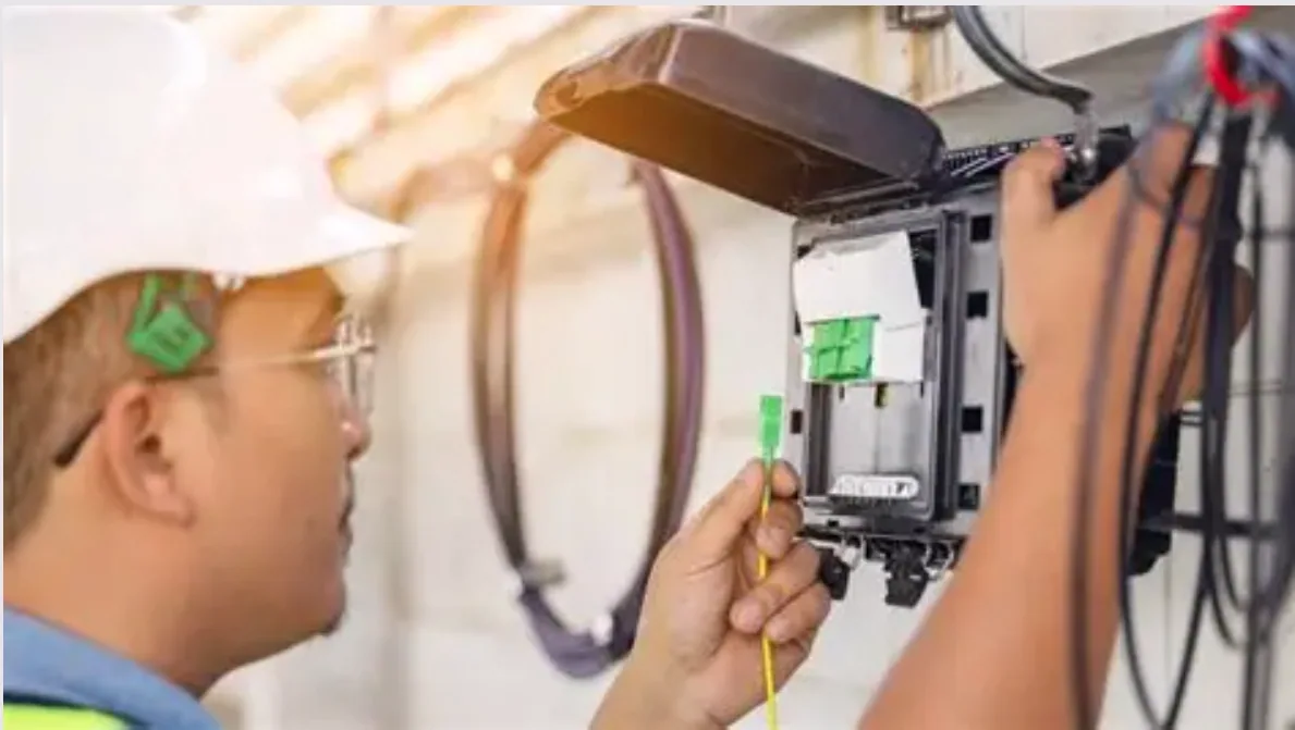Close-up of a fiber optic install—installer connects a yellow patch cord with a green connector to a distribution enclosure