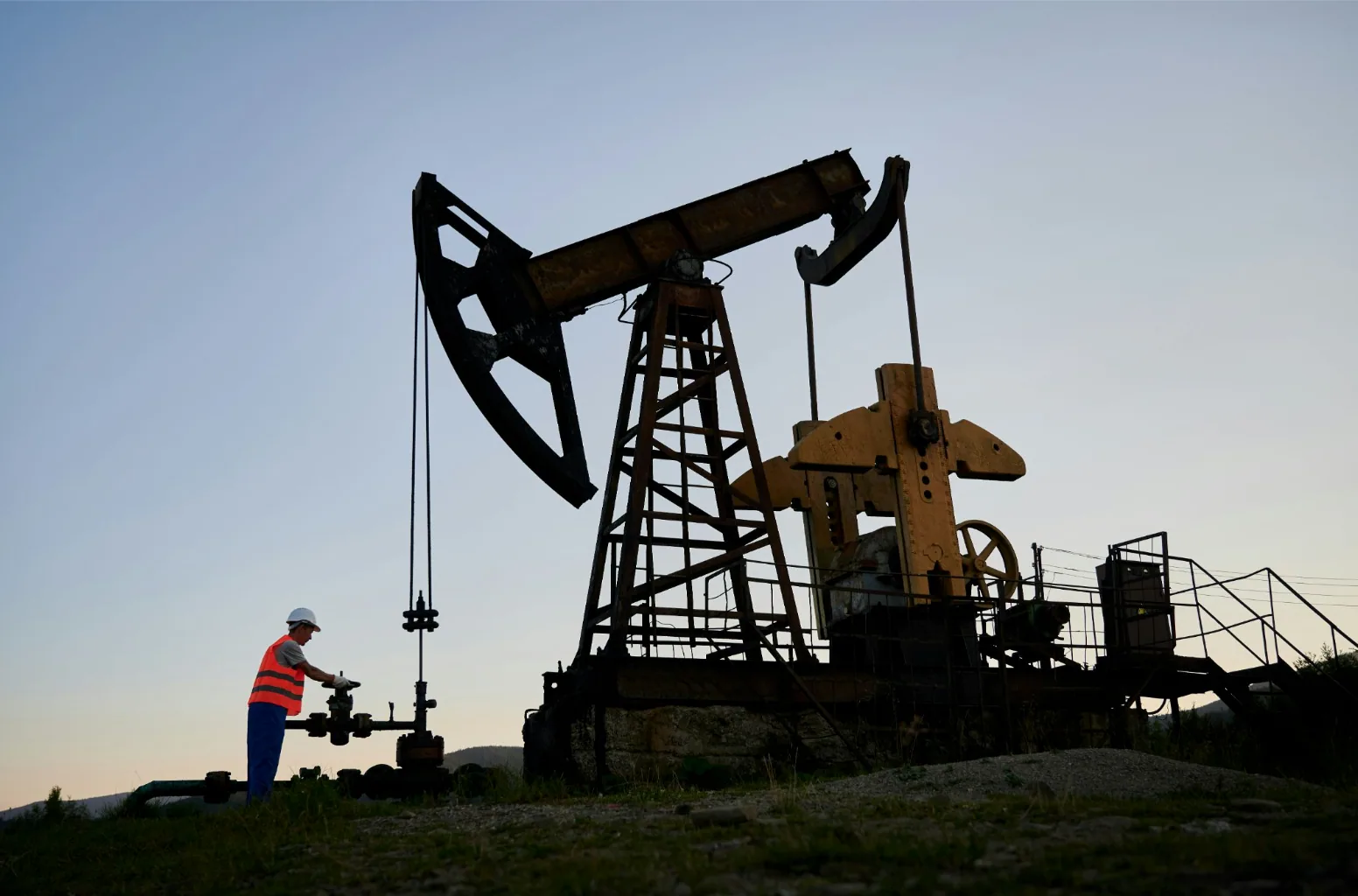 Oil field worker adjusting a pumpjack valve at dusk, representing the harsh conditions oil and gas industry cables must withstand.